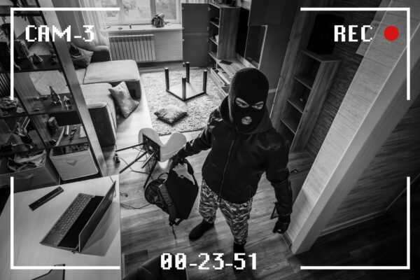 Surveillance screen capture showing a burglar wearing a mask in a house looking for valuables